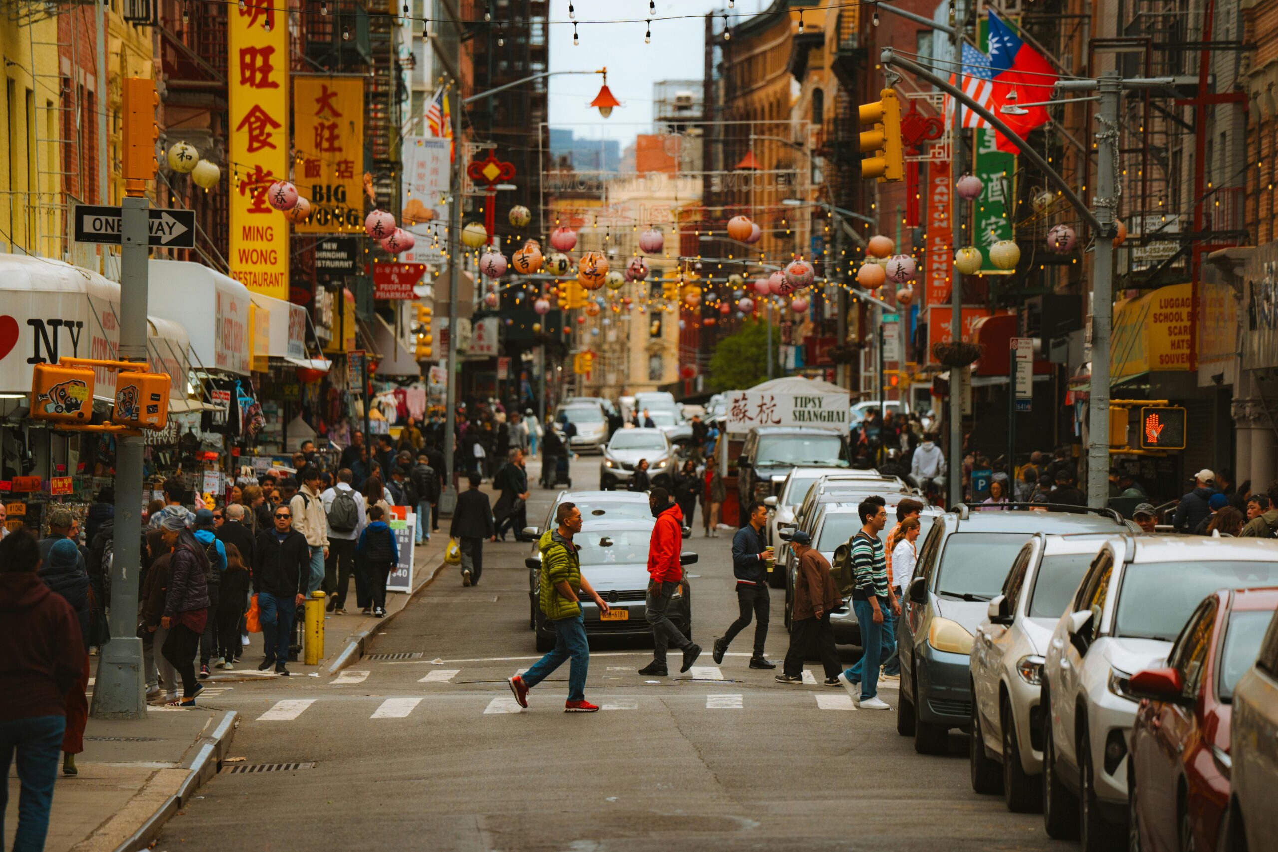 Lively urban scene in Chinatown with people walking and cars lining the street.