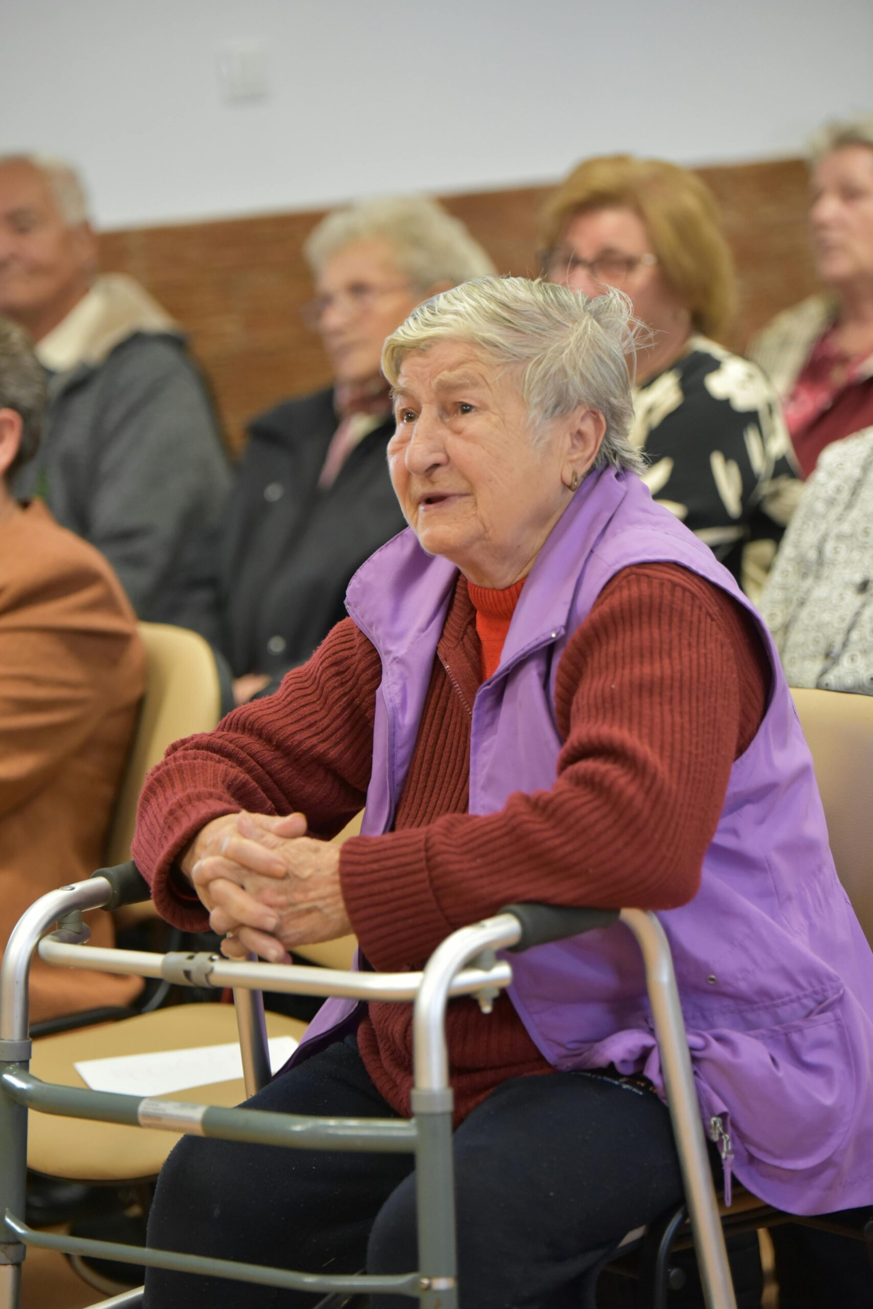 Senior woman with walker attending an indoor community meeting.
