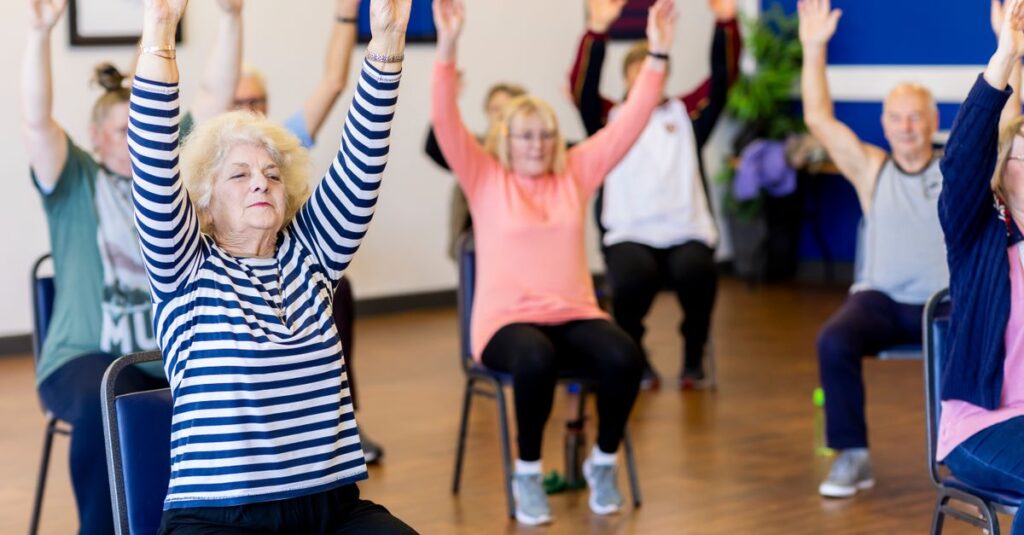 Group of senior adults participating in a chair exercise class, promoting fitness and healthy lifestyle.