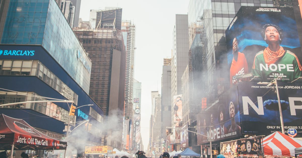 Crowds explore Times Square in New York City surrounded by skyscrapers, signs, and street vendors.