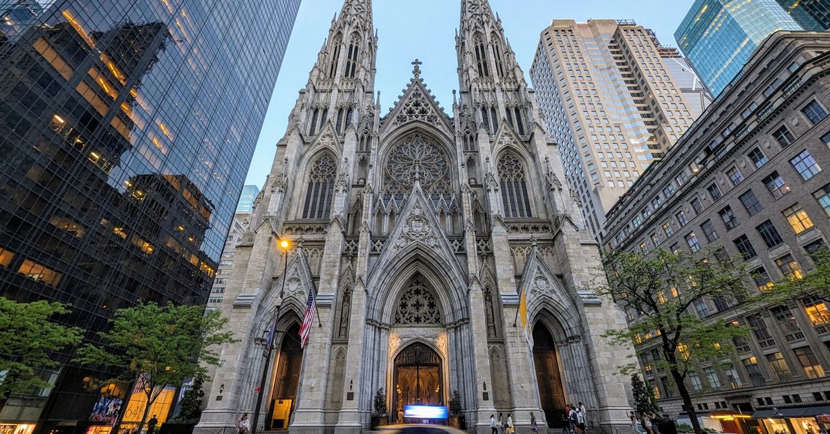 St. Patrick's Cathedral amidst New York skyscrapers with a taxi passing by at dusk.