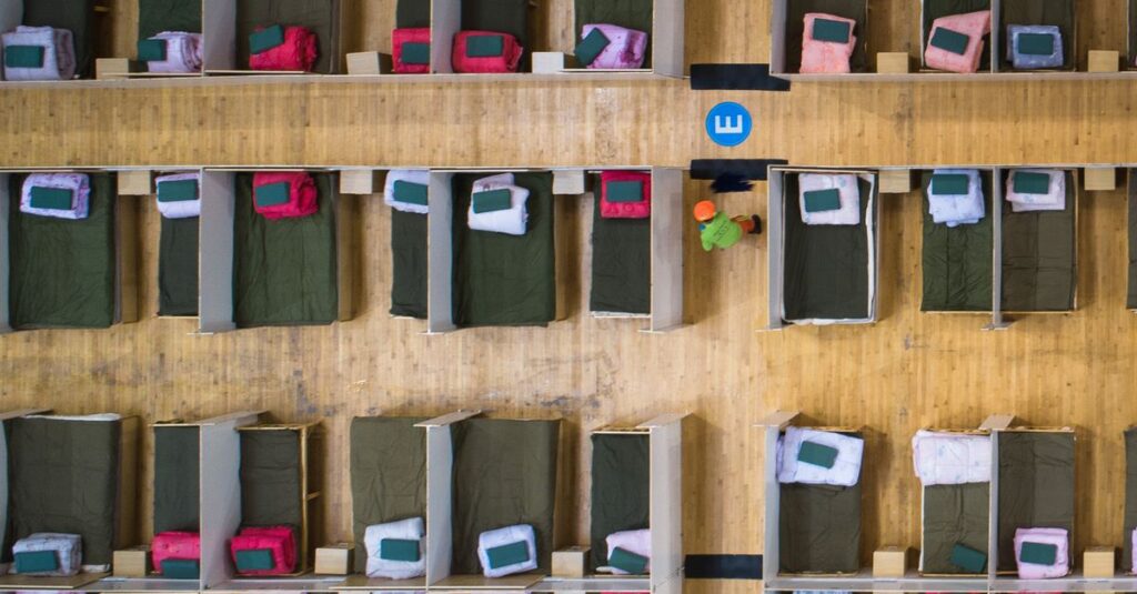 Top-down view of an emergency shelter with arranged beds in rows and worker present.