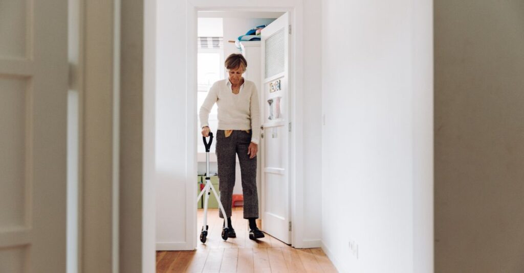 Senior woman walking with rollator in a brightly lit hallway for indoor mobility support.