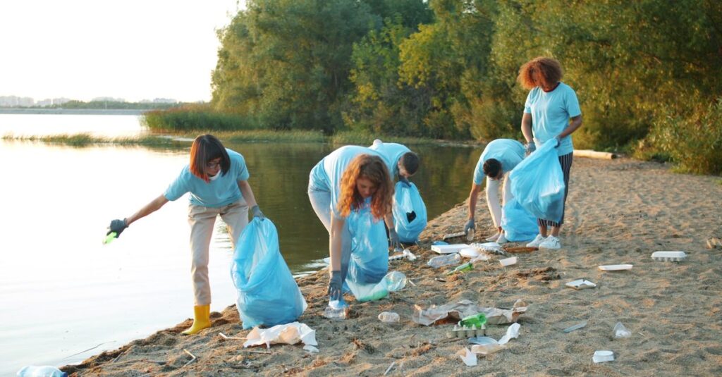 Group of volunteers cleaning a beach shoreline at sunset, promoting environmental awareness.