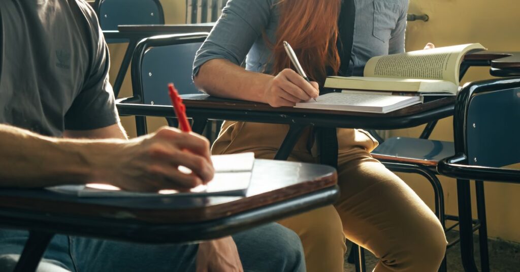 Two students writing notes in a classroom setting, focusing on study and education