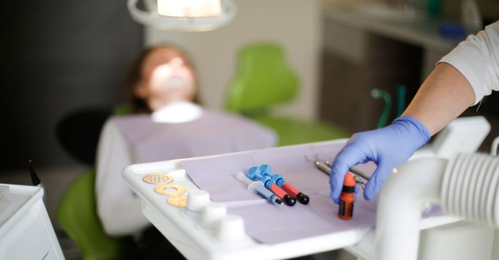Crop dentist in blue rubber medical gloves curing teeth to patient in modern hospital office