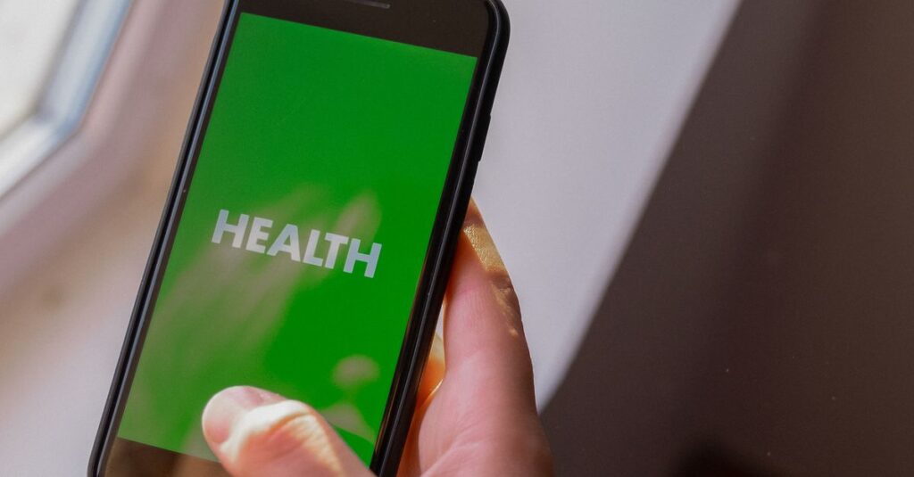 Close-up of a hand holding a smartphone displaying the word 'Health' on a green screen.