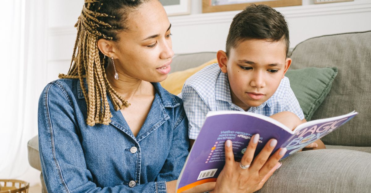 A mother reading a book with her young son on a comfortable couch indoors.