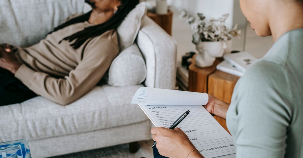 Crop anonymous African American female with paper form talking to male partner during psychotherapy in living room