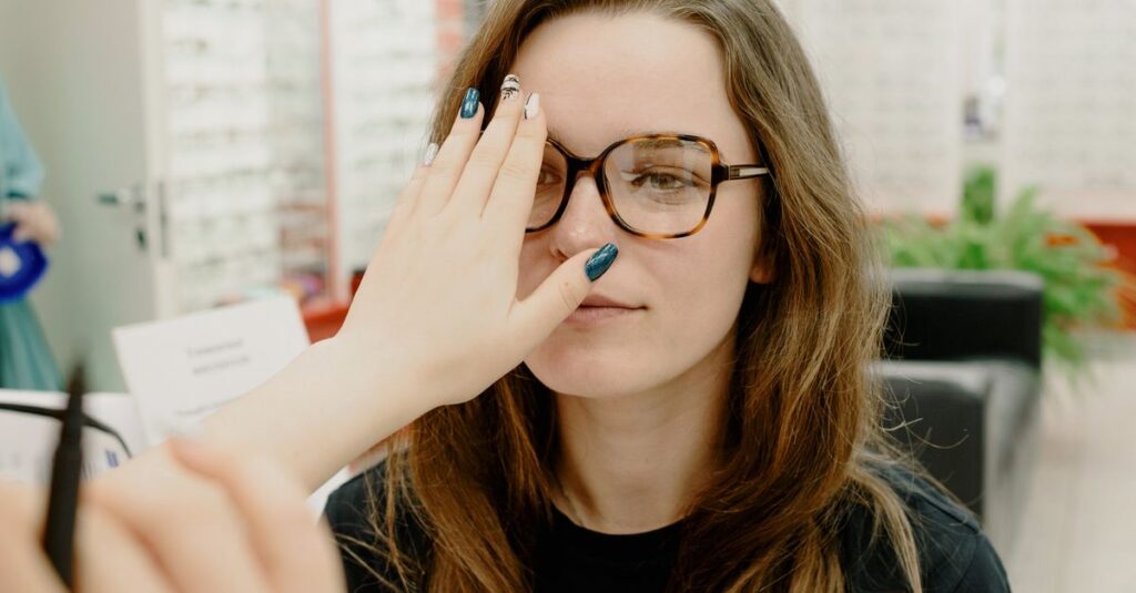 Focused female patient looking at hand of unrecognizable ophthalmologist while checking eyesight in new eyeglasses during appointment in clinic on blurred background