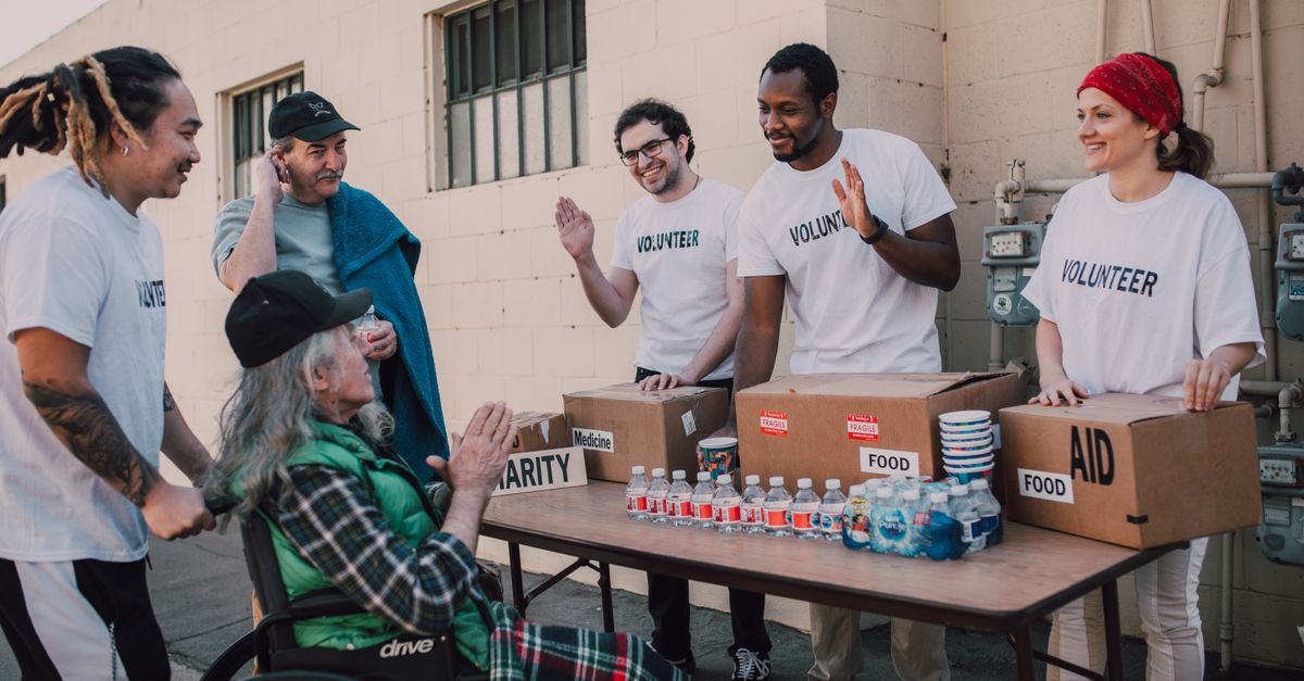 Group of volunteers providing food and aid to a person in wheelchair outdoors.