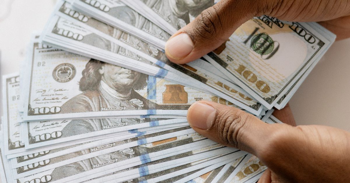 Close-up view of hands counting U.S. hundred dollar bills over a laptop background.