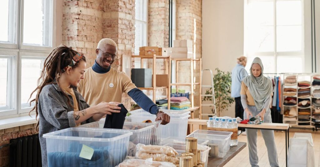 A diverse group of young adults volunteering at a donation center sorting clothes.