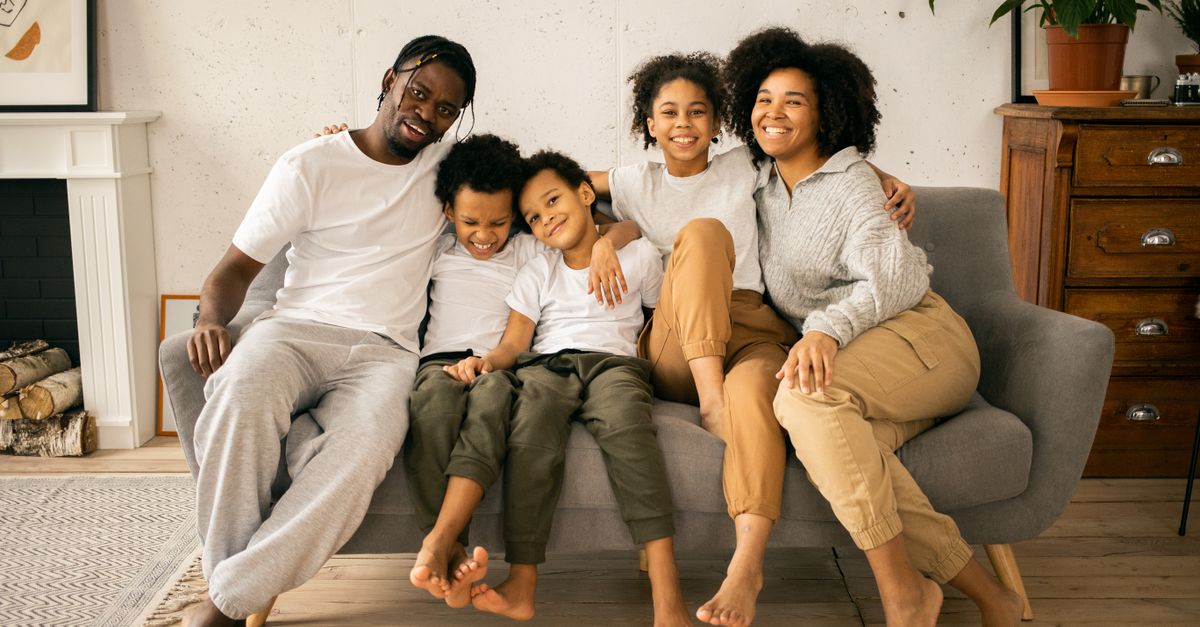 Full body of cheerful African American parents with children looking at camera while sitting on sofa in room with fireplace