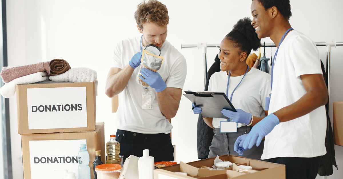 Three diverse volunteers sorting donation boxes filled with clothing and supplies indoors.
