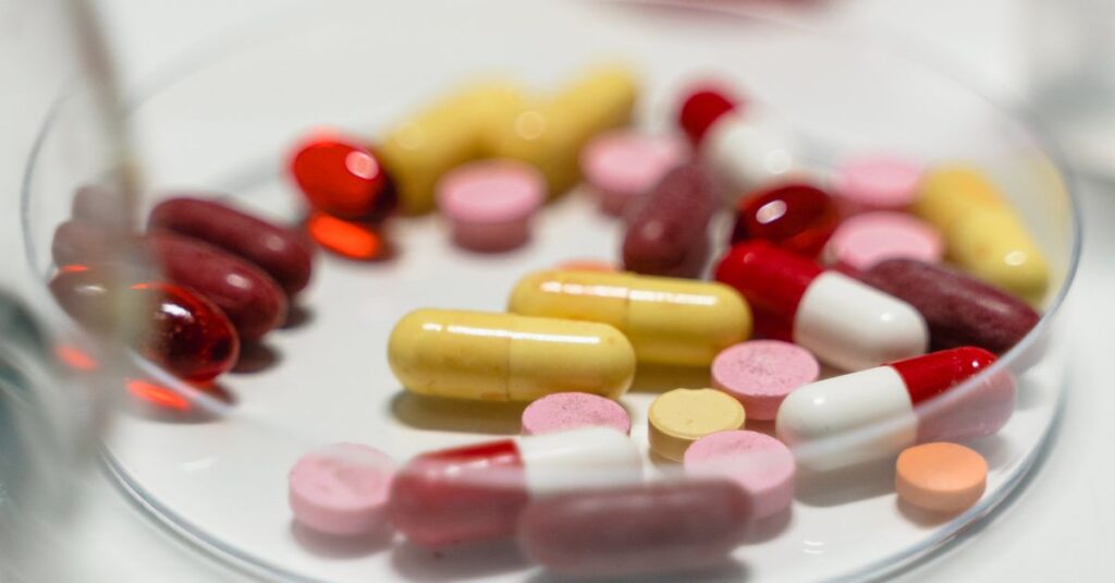 Assorted colorful pills and capsules arranged on a Petri dish for pharmaceutical analysis.