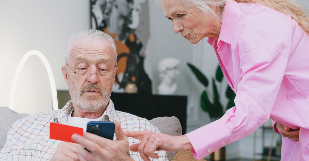 Elderly couple handling credit card transaction on smartphone indoors.