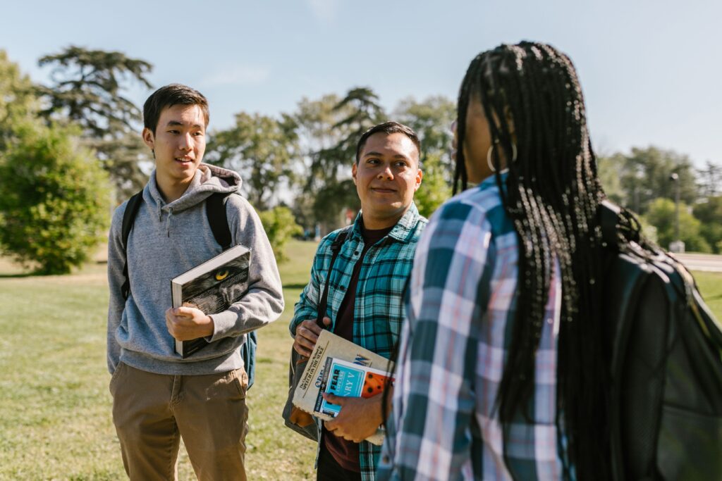 Group of students chatting outdoors with books on a sunny day.