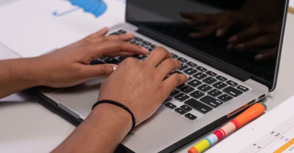 A person works on a laptop with colorful markers and a printed chart nearby.