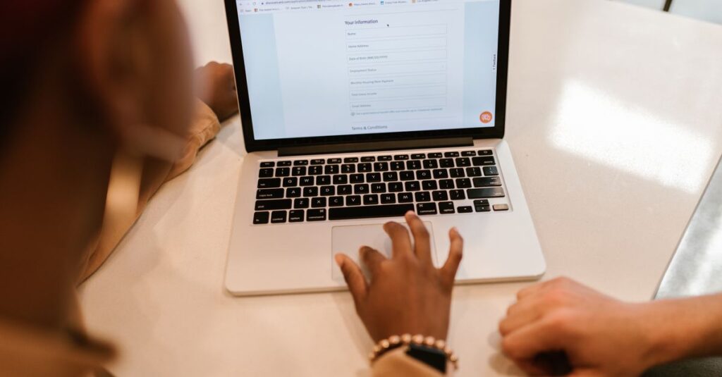 Two adults working together on a laptop displaying an online form, indoors.