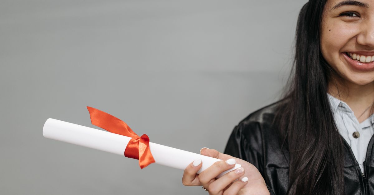 A happy female graduate smiles while holding a diploma tied with a red ribbon.
