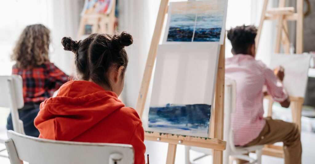 Children engaged in a creative art class, painting on easels indoors.