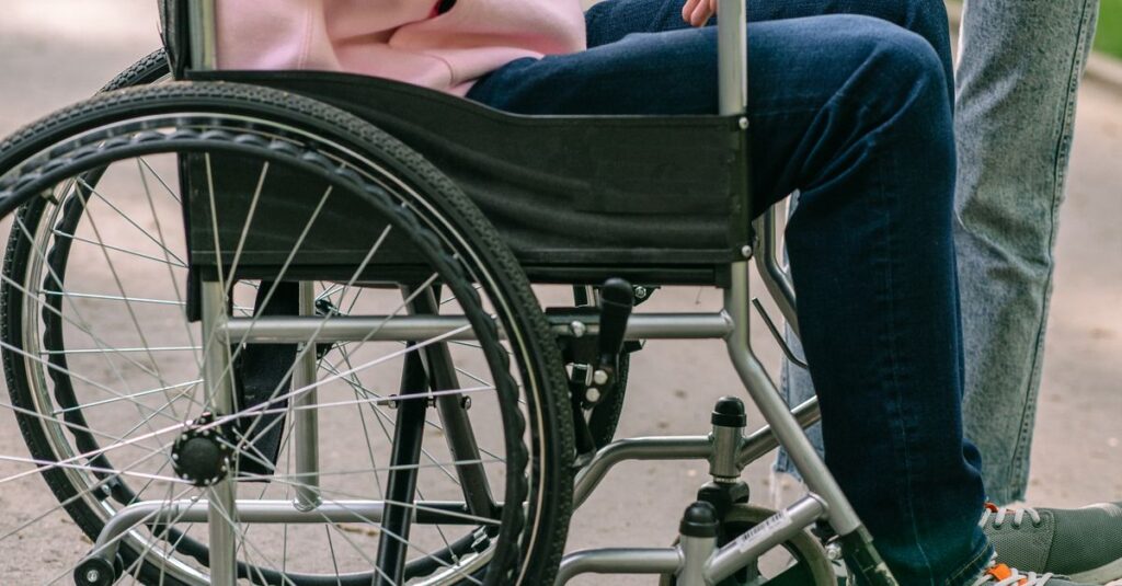 Person in wheelchair holding hands with another individual, showing support and compassion outdoors.