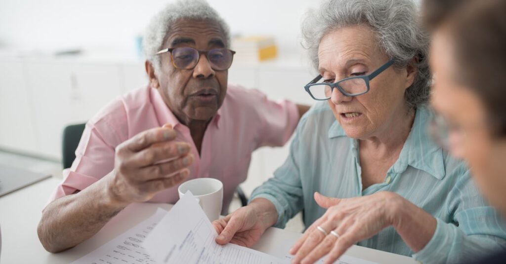 Elderly couple discussing financial documents with a consultant in an office setting.