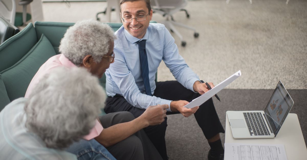 Consultant discussing financial plans with senior clients in a modern office setting, using documents and a laptop.