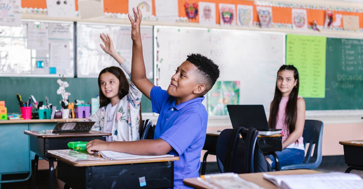 Children in a lively classroom raising hands during an interactive lesson.