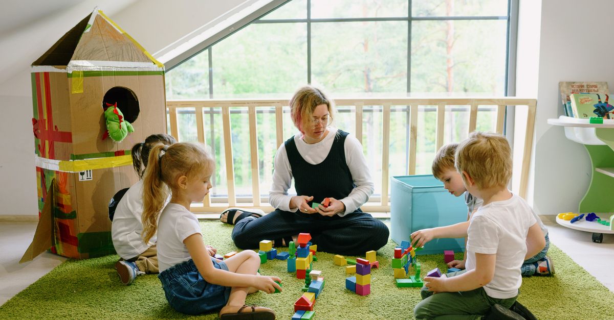 Children enjoying playtime with blocks and cardboard house in a cozy classroom.