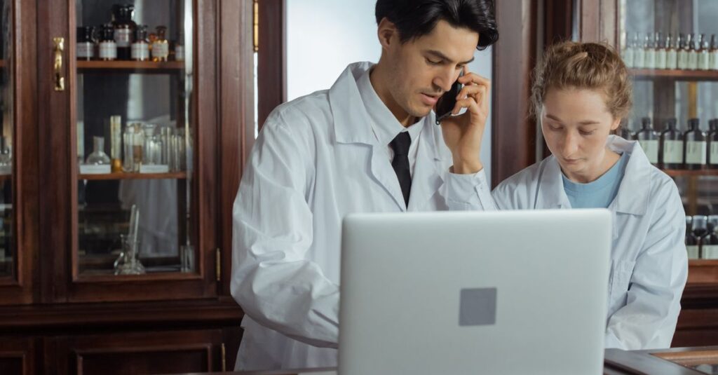 Two pharmacists working together in a pharmacy, using a laptop and phone for efficient operations.