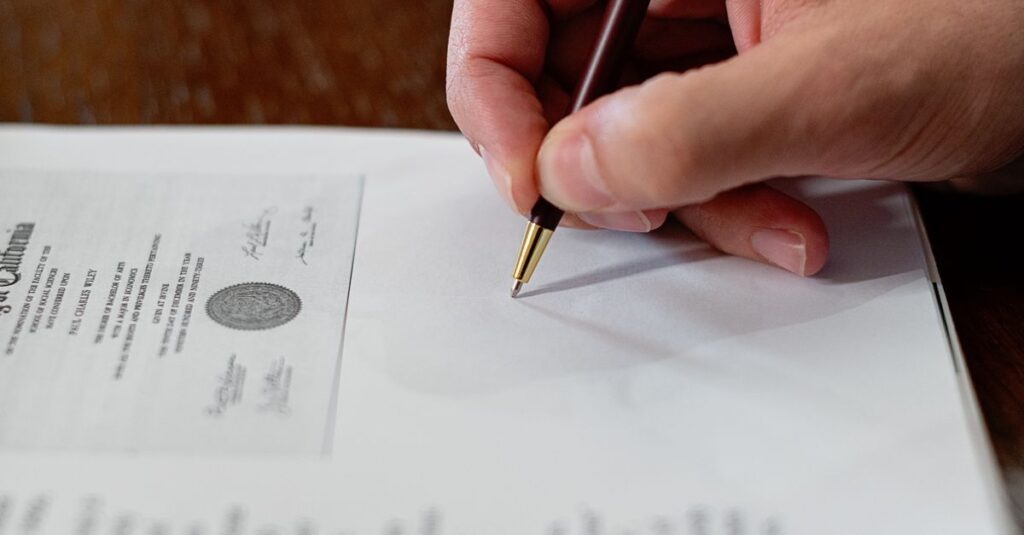 A detailed close-up photo of a hand signing a formal document with a pen, creating a professional agreement.