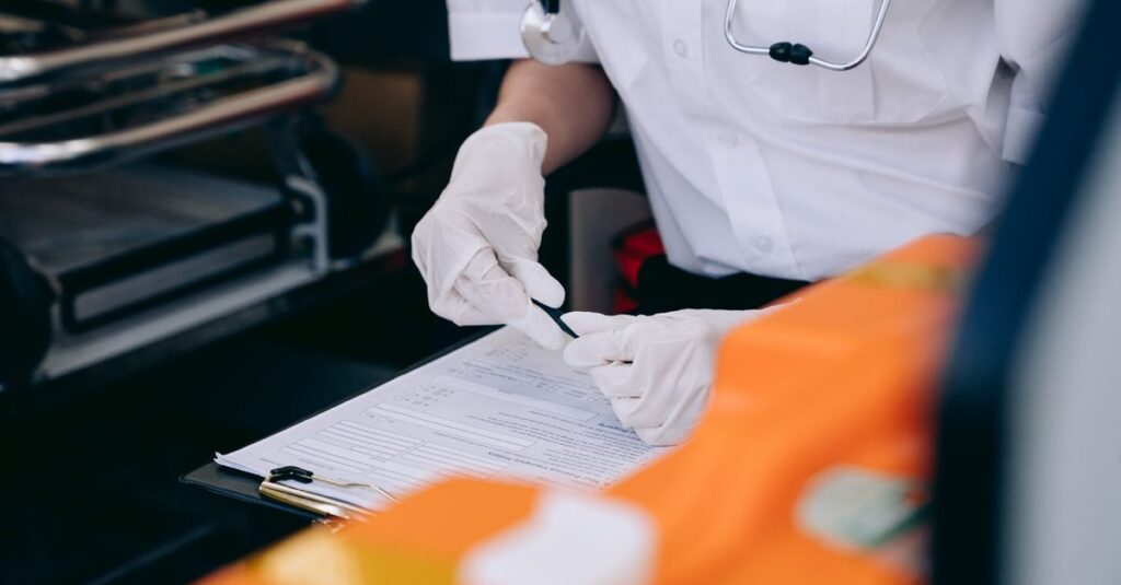 A medic wearing gloves and a stethoscope takes notes inside an ambulance.
