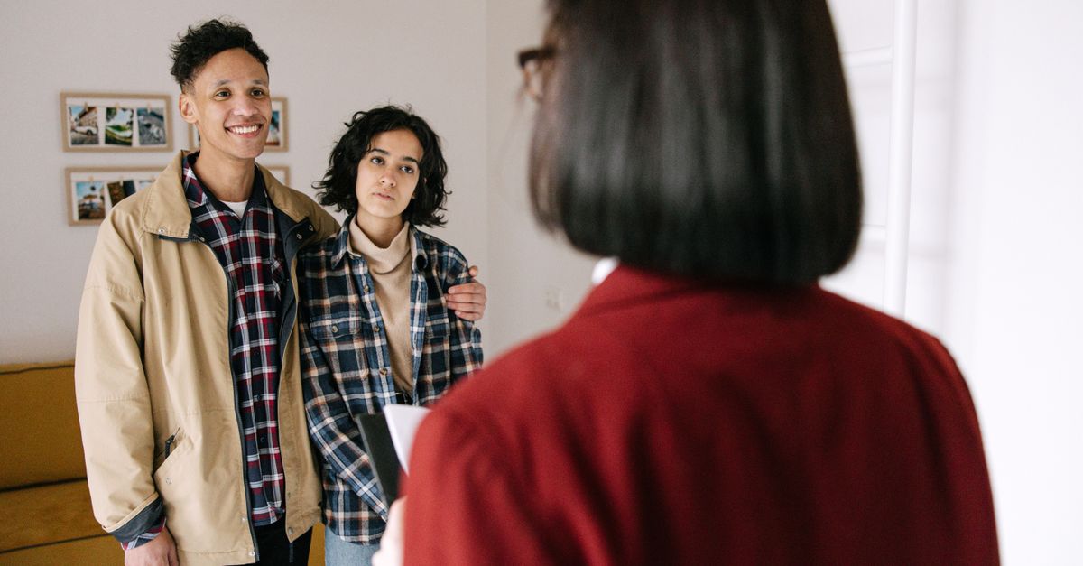 Young couple discussing real estate options with an agent indoors, highlighting home buying process.