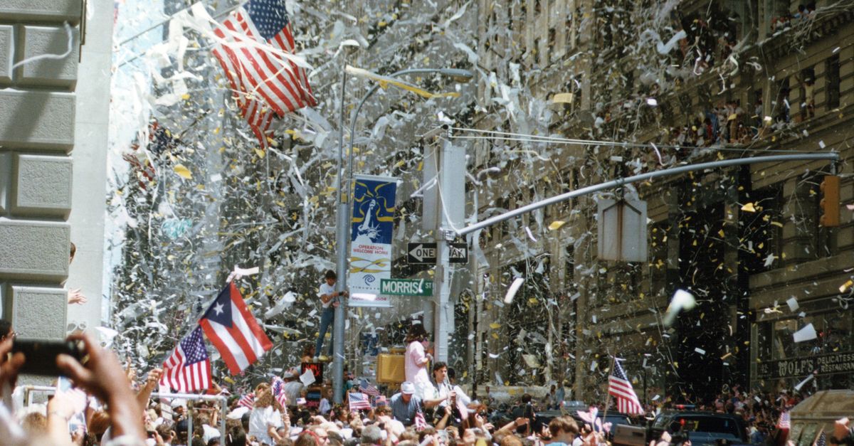 Lively street parade in New York City with confetti, flags, and cheering crowd.