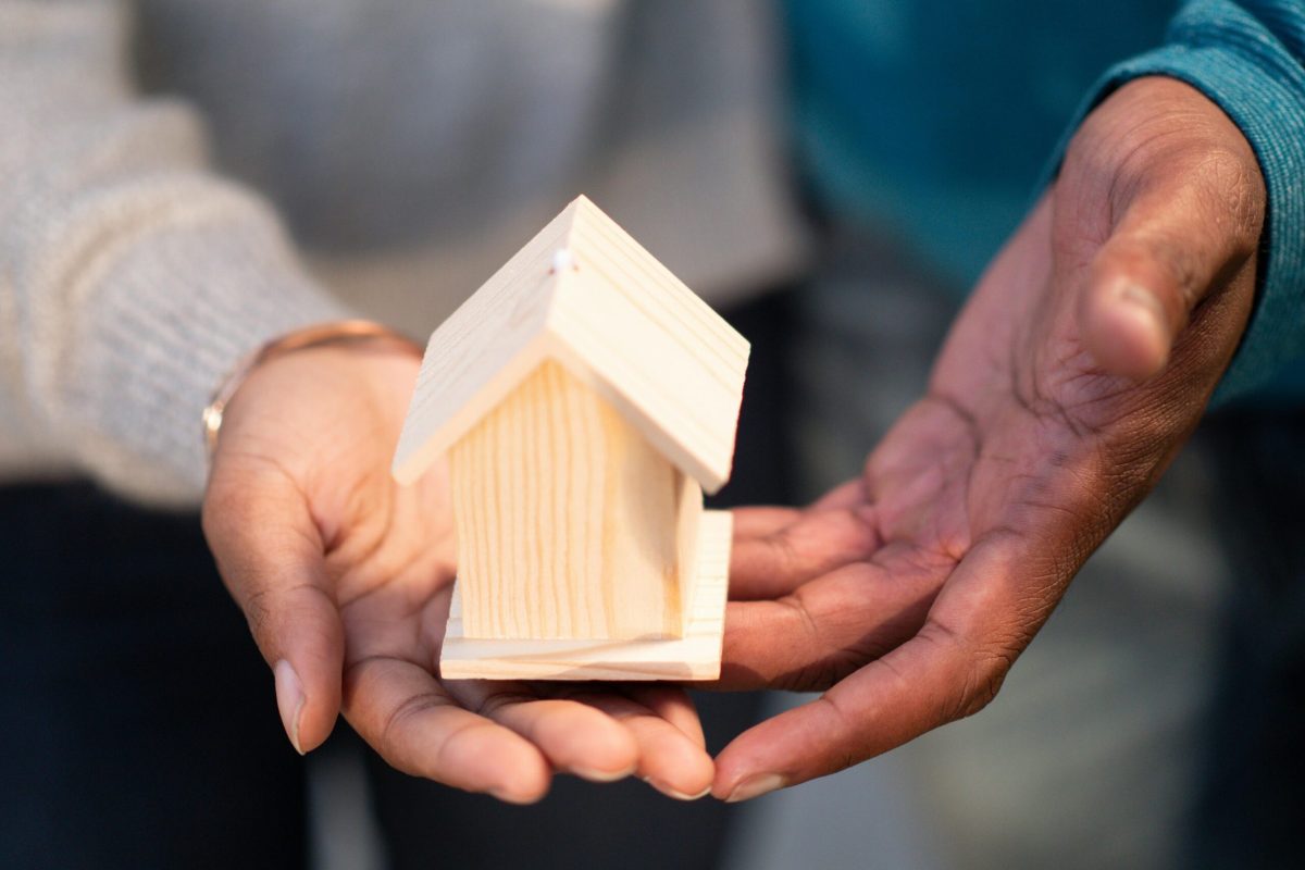 Hands holding a small wooden house model, symbolizing new home ownership and real estate transactions.